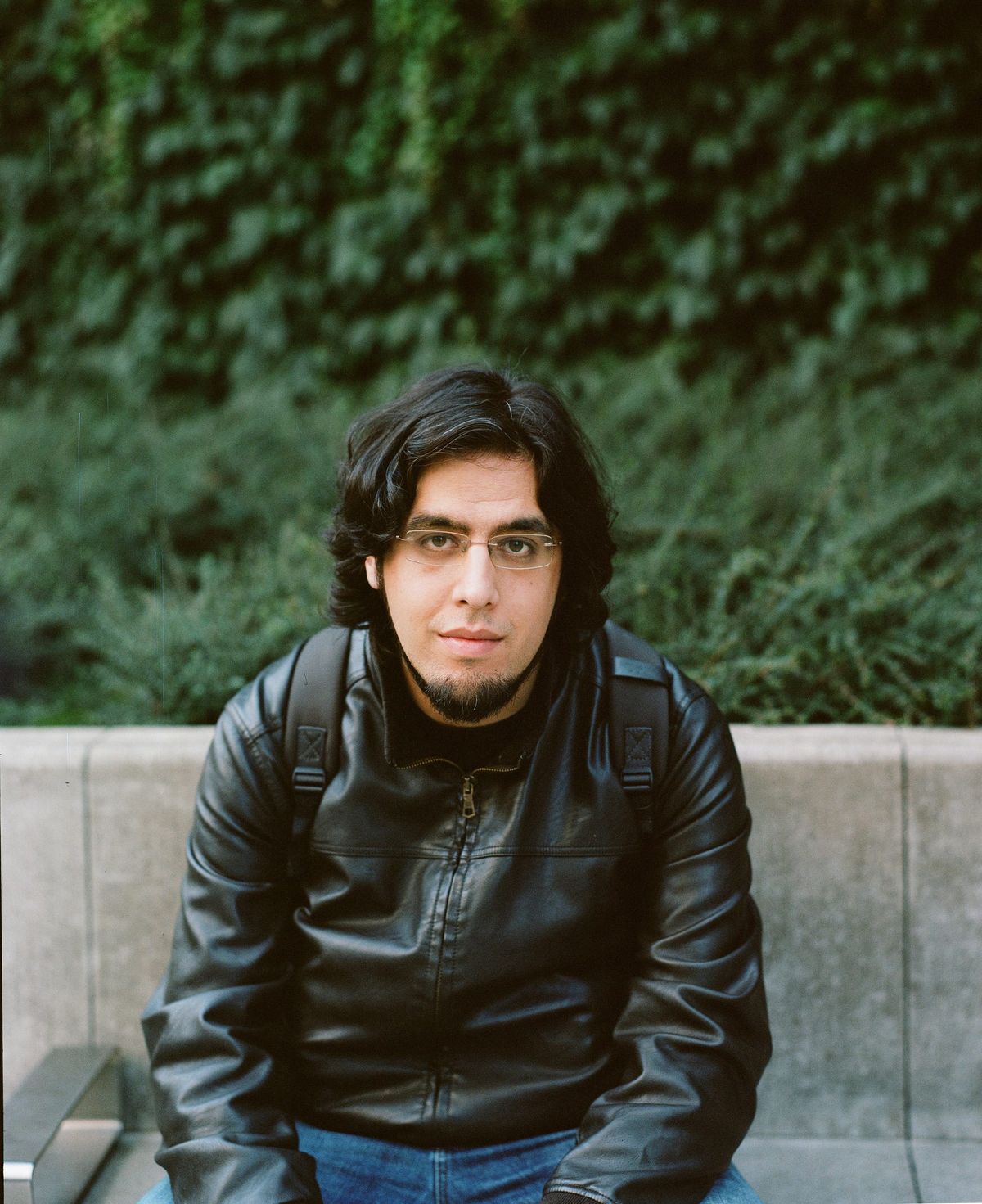 Rami Ismail seated in a leather jacket against a low concrete wall