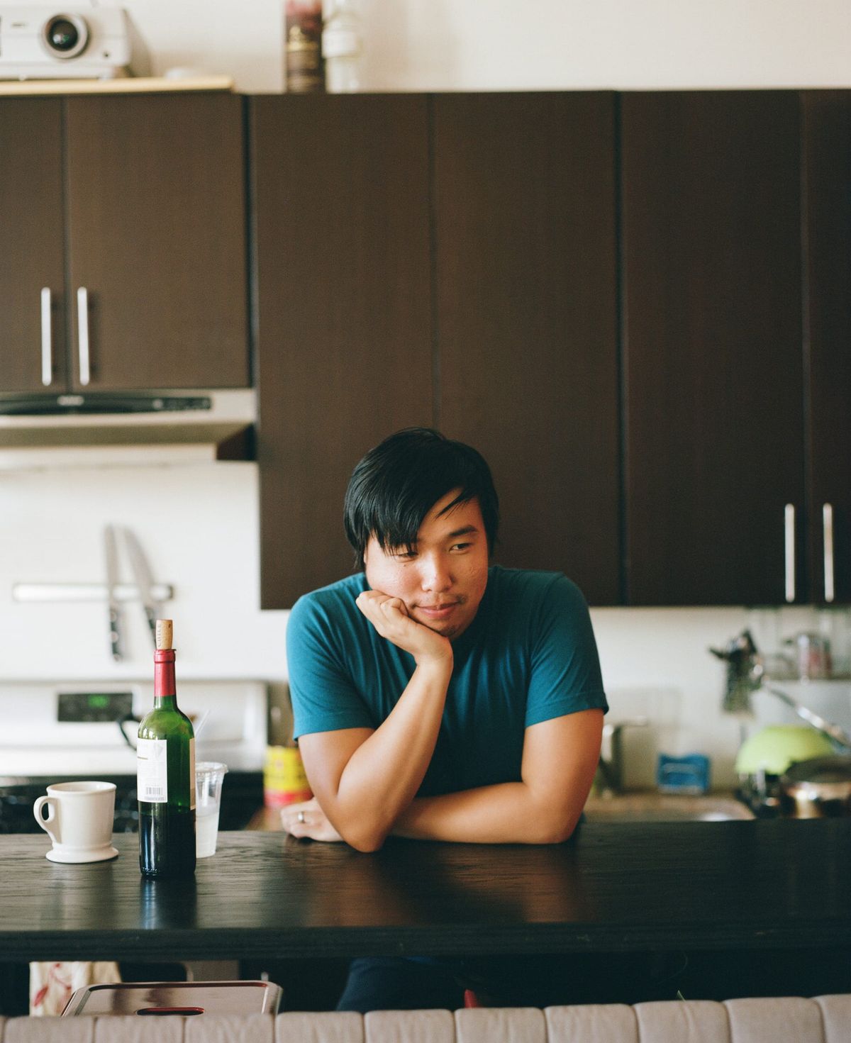 Robert Yang leaning on a kitchen counter with a wine bottle and mug beside him