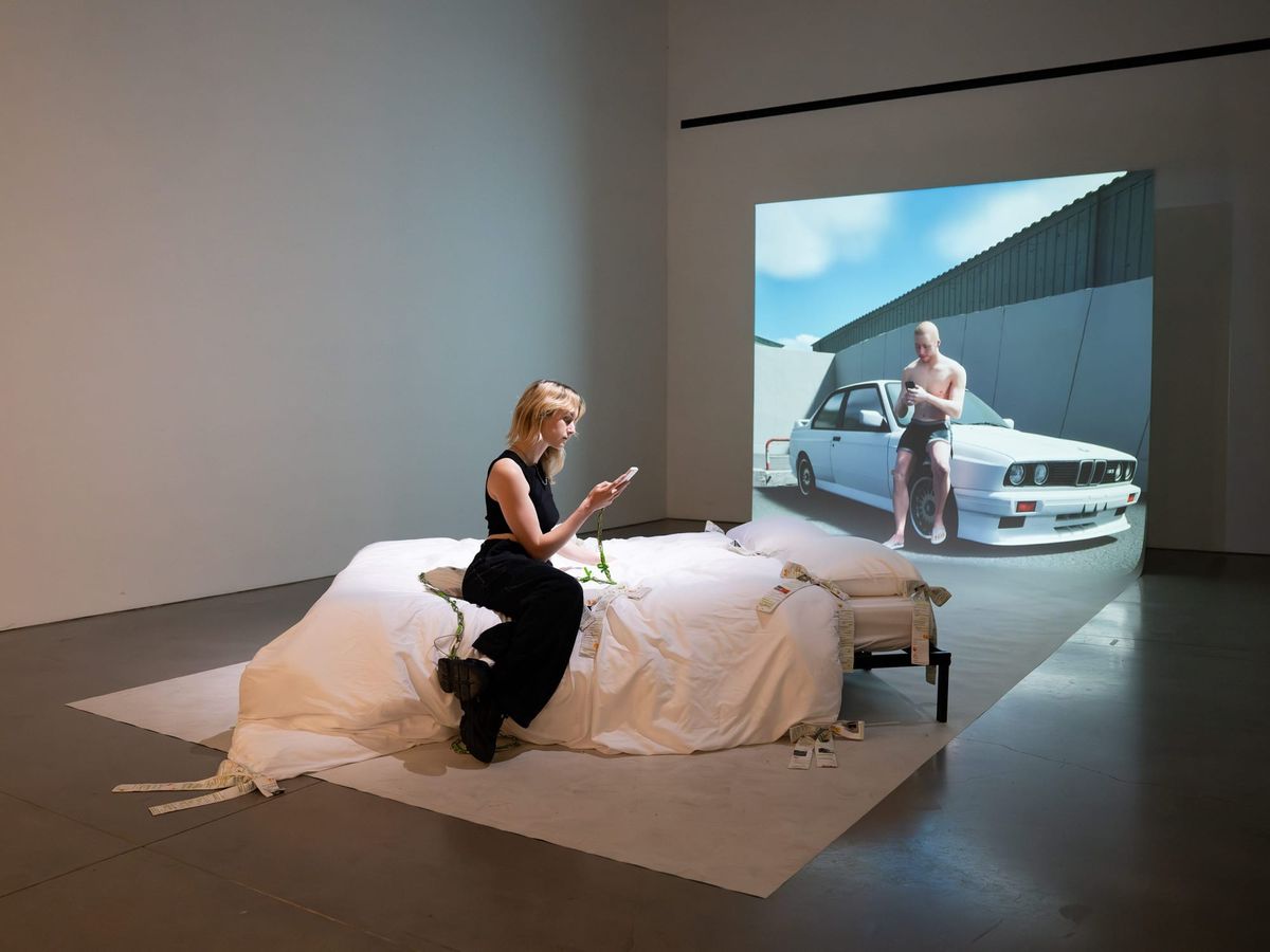 Installation view of Abel & I: a bed facing a large projection of the synthetic character Abel