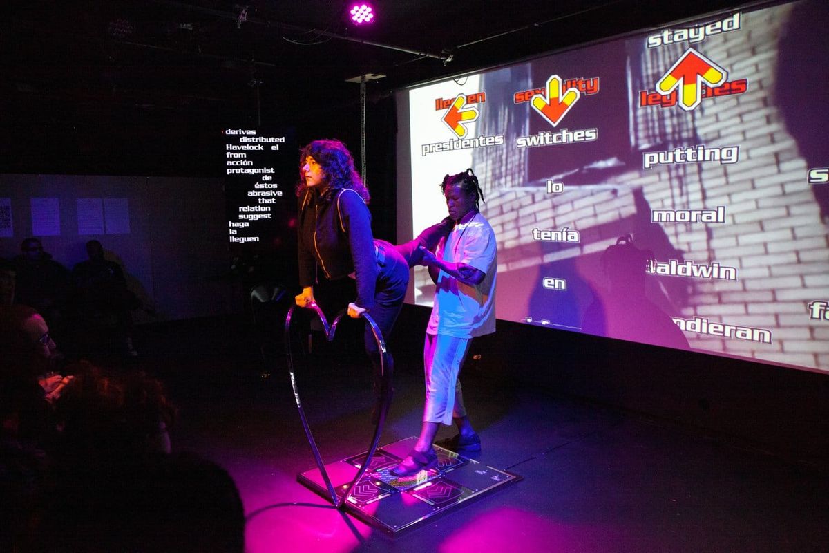 Two performers on a dance pad in front of a projected screen of arrows and words
