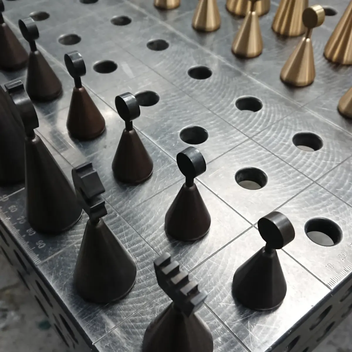 Brass chess pieces shaped as small bells standing in the holes of a perforated metal board