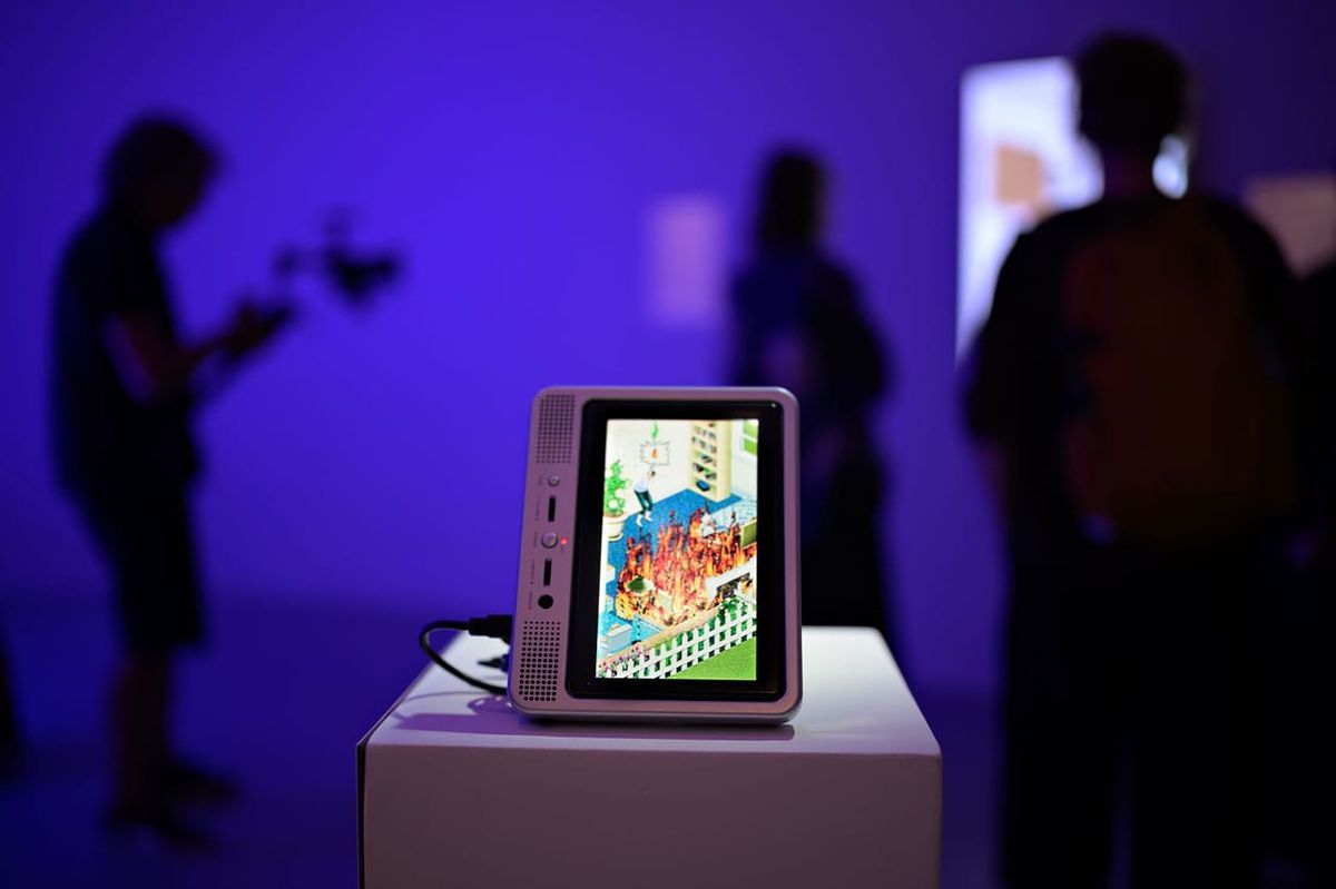 A portable DVD player on a white plinth shows a Sims house surrounded by flames, with visitors in silhouette behind it