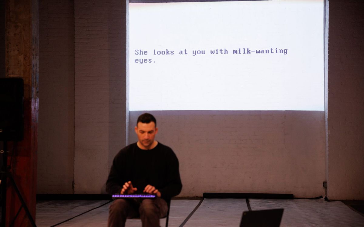Matt Romein seated at a keyboard in a black box theater, with a line of game text projected on the wall behind