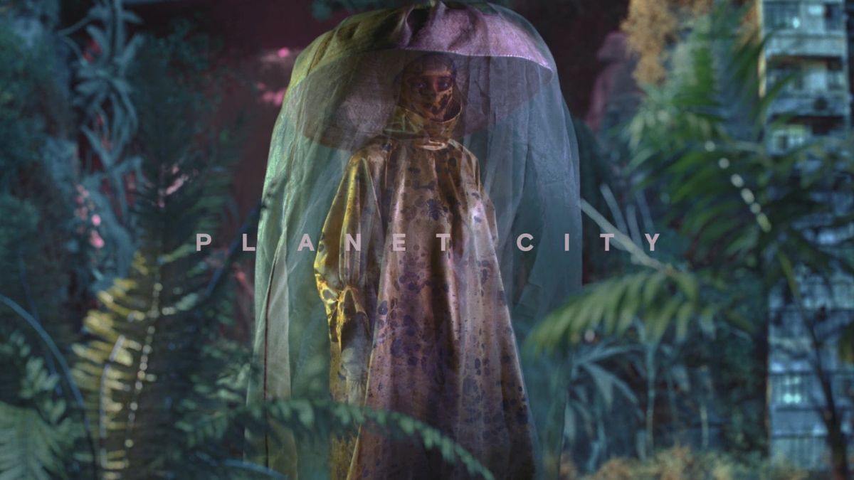 A figure in a translucent veil and elaborate costume stands among dense jungle plants, with the words Planet City across the frame