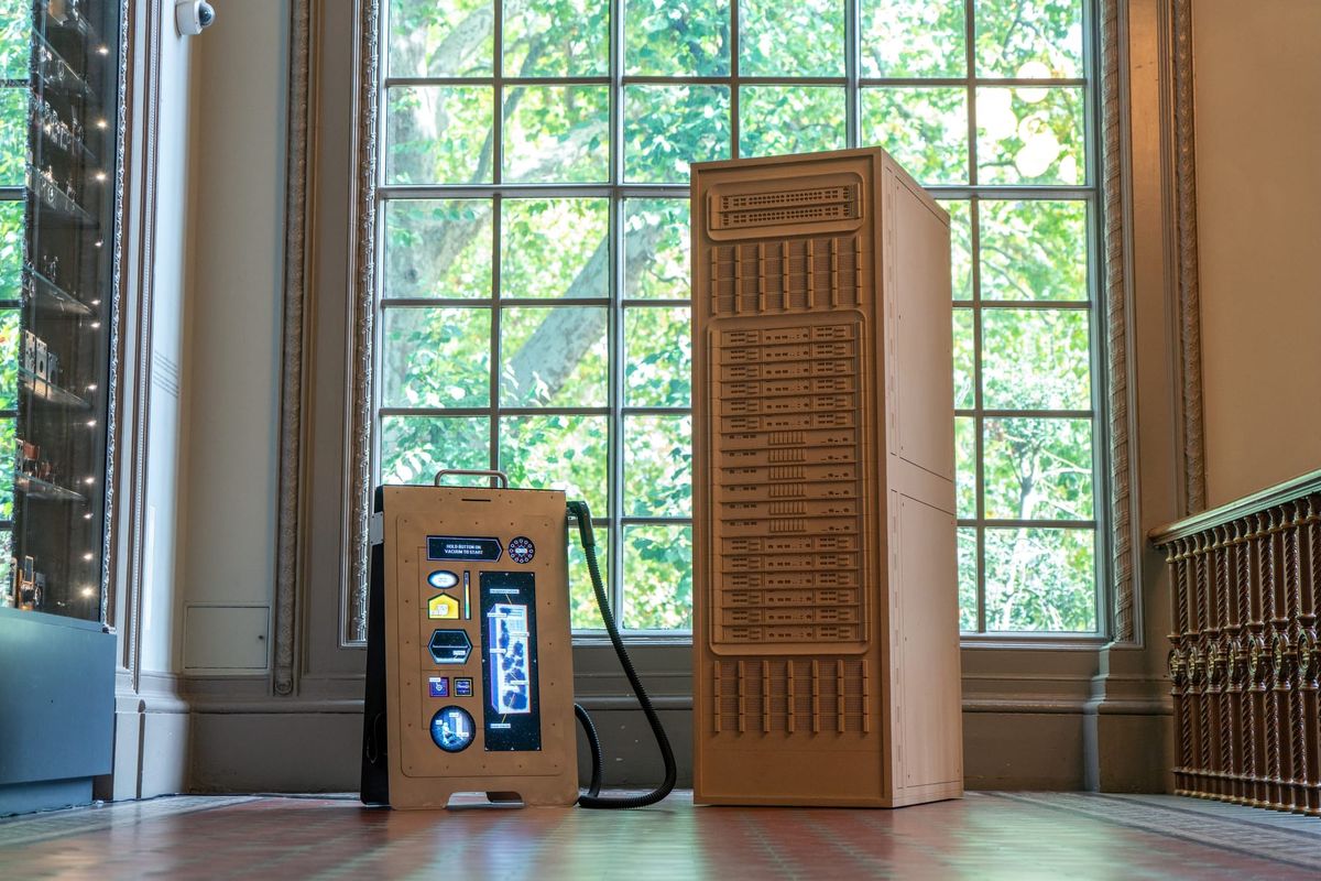 A wooden server tower installation with a data-centre vacuum beside tall museum windows