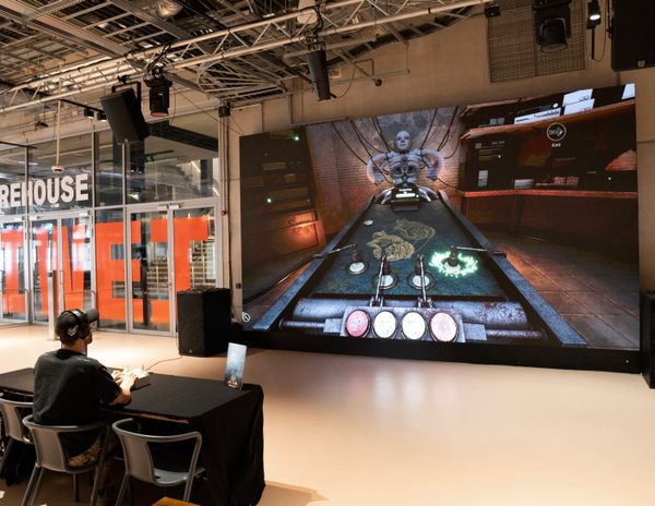 A player at a table uses a custom controller in front of the Media Wall showing Something Beautiful at Aviva Studios