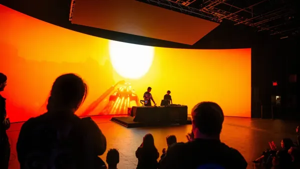 Performer operating a sculptural camera controller in front of a projected synthetic forest