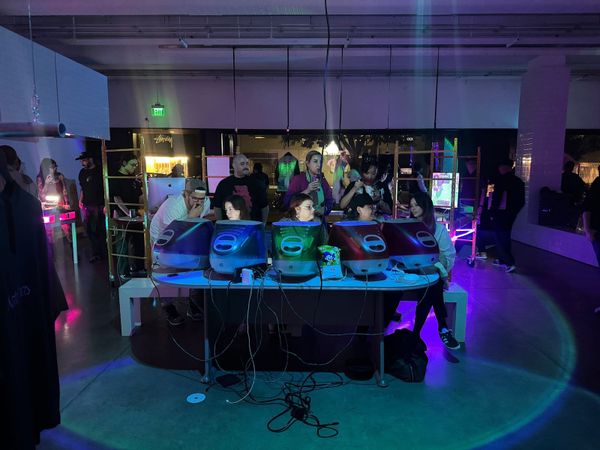 Attendees seated at a long table of colorful vintage iMac G3 computers at a Dead Internet Theory party