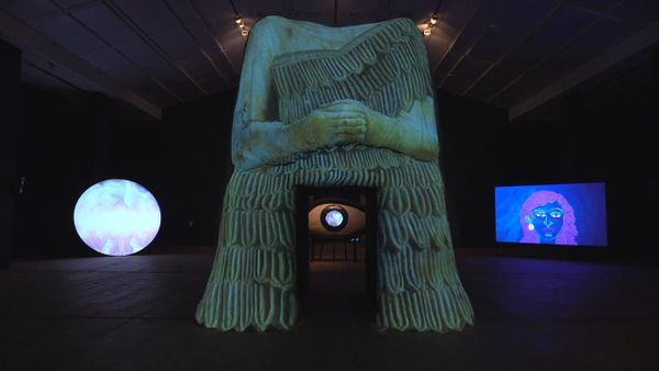 A monumental headless votive figure with a glowing projected eye in its doorway, at BALTIC