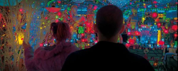 Two figures seen from behind looking out over a dense field of multicolored neon signs