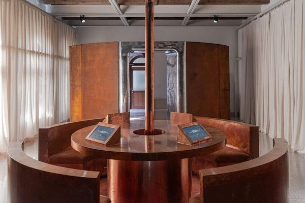 Circular copper bench and table with embedded screens under a copper column in a curtained gallery