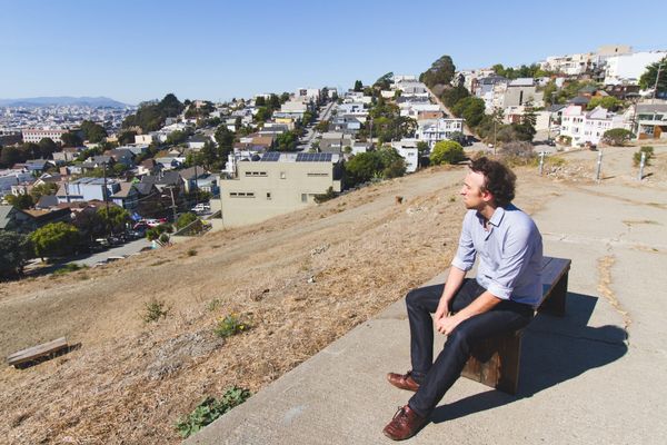 Marc ten Bosch sits on a wooden bench atop a dry hillside, looking out over San Francisco