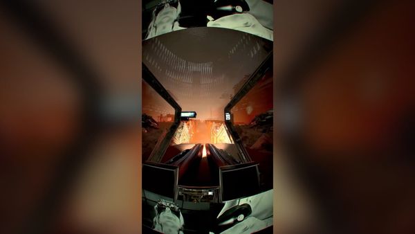Point-of-view shot from inside a fisheye-warped racing cockpit, banks of monitors below the windshield and a fiery orange horizon ahead.