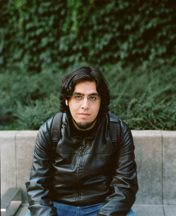 Rami Ismail seated in a leather jacket against a low concrete wall