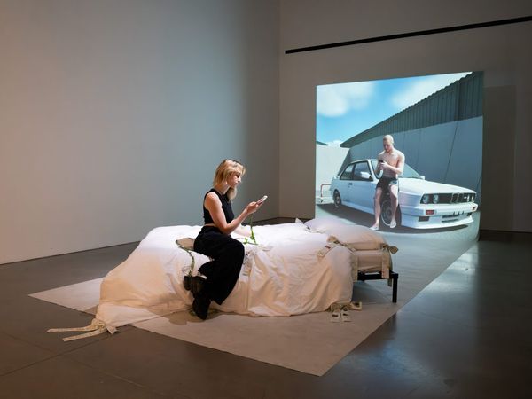 Installation view of Abel & I: a bed facing a large projection of the synthetic character Abel