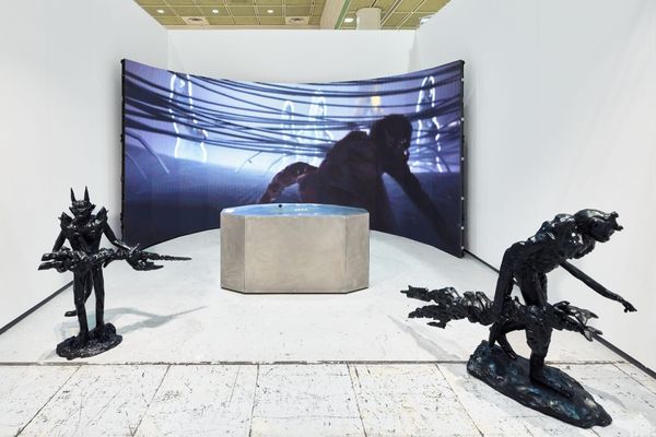 Two black sculptures flank a concrete plinth before a curved screen in Gabriel Massan's ANIMA KINESIS