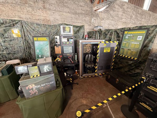 The Big Steel Battalion Box cockpit at Maker Faire Bay Area 2026, its open hatch showing the pilot's seat inside a camouflage-draped booth
