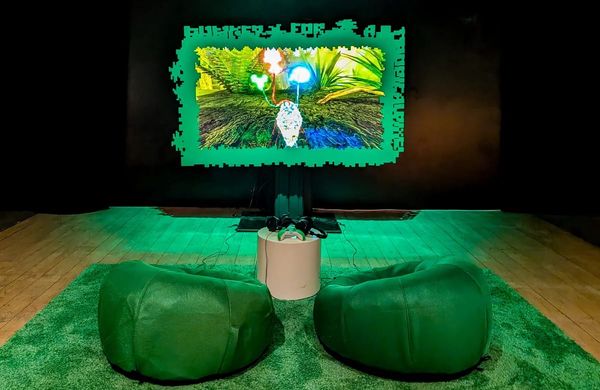 A game projected inside a green frame over green carpet and two green floor seats in a dark room