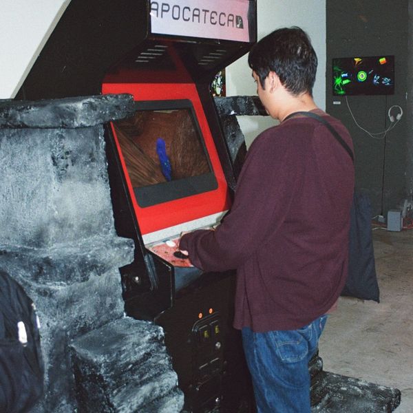 A visitor plays the red Ex-Nihilo ii arcade cabinet in a darkened gallery