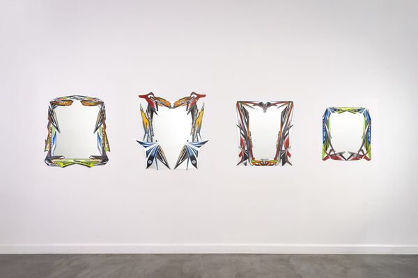 Four wall mirrors framed in colorful decal-covered scooter body panels, hung in a row on a white gallery wall.
