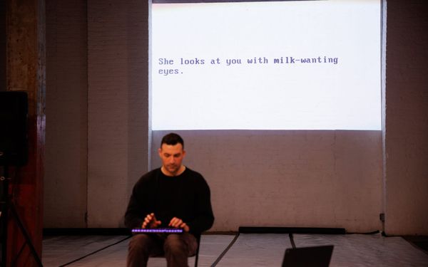 Matt Romein seated at a keyboard in a black box theater, with a line of game text projected on the wall behind