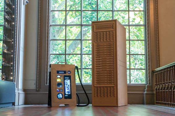 A wooden server tower installation with a data-centre vacuum beside tall museum windows