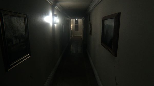 A dim, narrow hallway with framed pictures on both walls and a single bright wall lamp, the corridor from the game P.T.