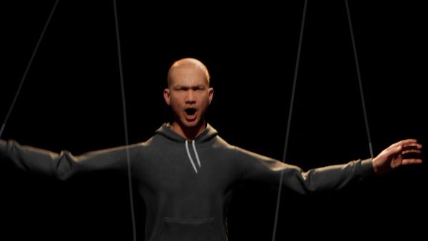 A 3D figure in a black hoodie hangs from marionette strings, arms outstretched, in the installation PUPPET