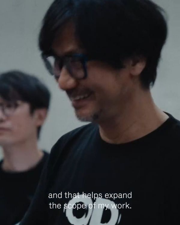Hideo Kojima smiling in a studio, wearing a black T-shirt, in a still from a Rimowa campaign film.