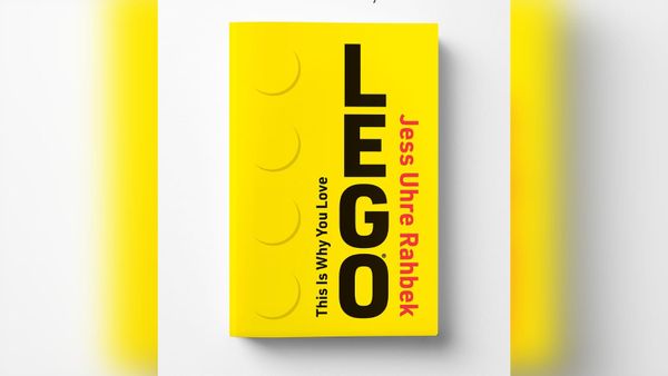 The yellow cover of This Is Why You Love LEGO by Jess Uhre Rahbek, styled like a LEGO brick seen from the side.
