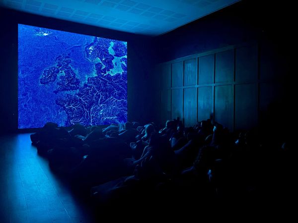 An audience lies back in a dark hall beneath large blue projections of flowing water