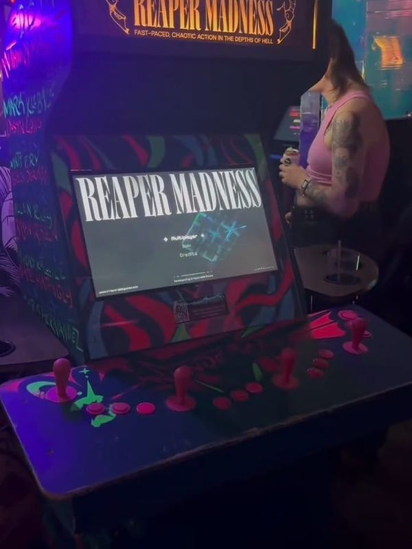 An arcade cabinet marked Reaper Madness glows in the dark interior of the Wonderville bar