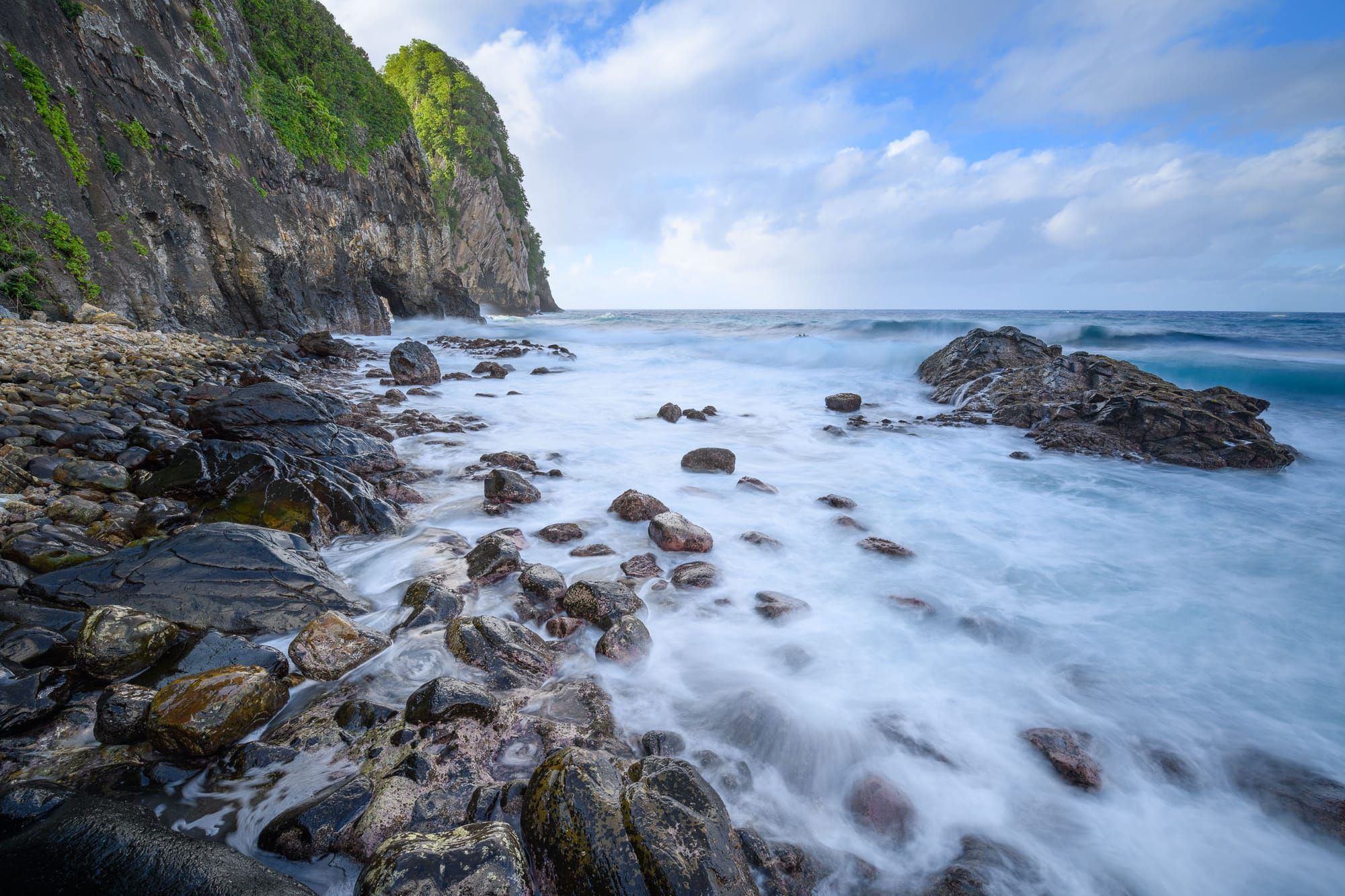 Rocky shoreline of the Vatia Coast in the National Park of American Samoa, with waves crashing against r under a cloudy sky.