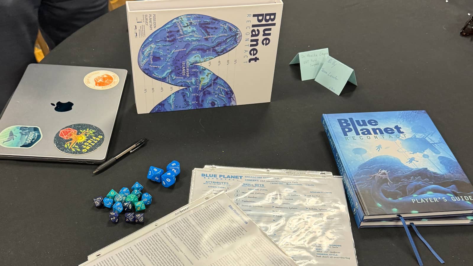On the game table, the Blue Planet slipcase (which contains two core books), bunches of d10 dice, and laminated character sheets and cheat sheets..