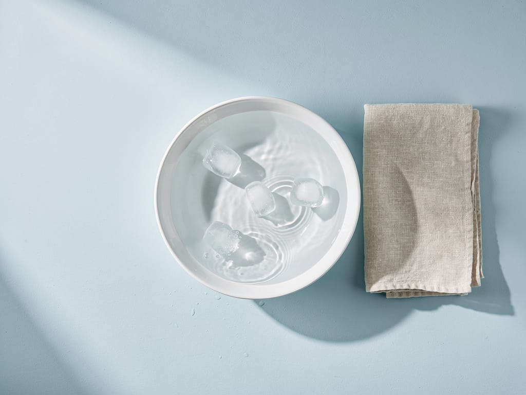 Ceramic bowl with cold water and ice cubes on a clean white surface