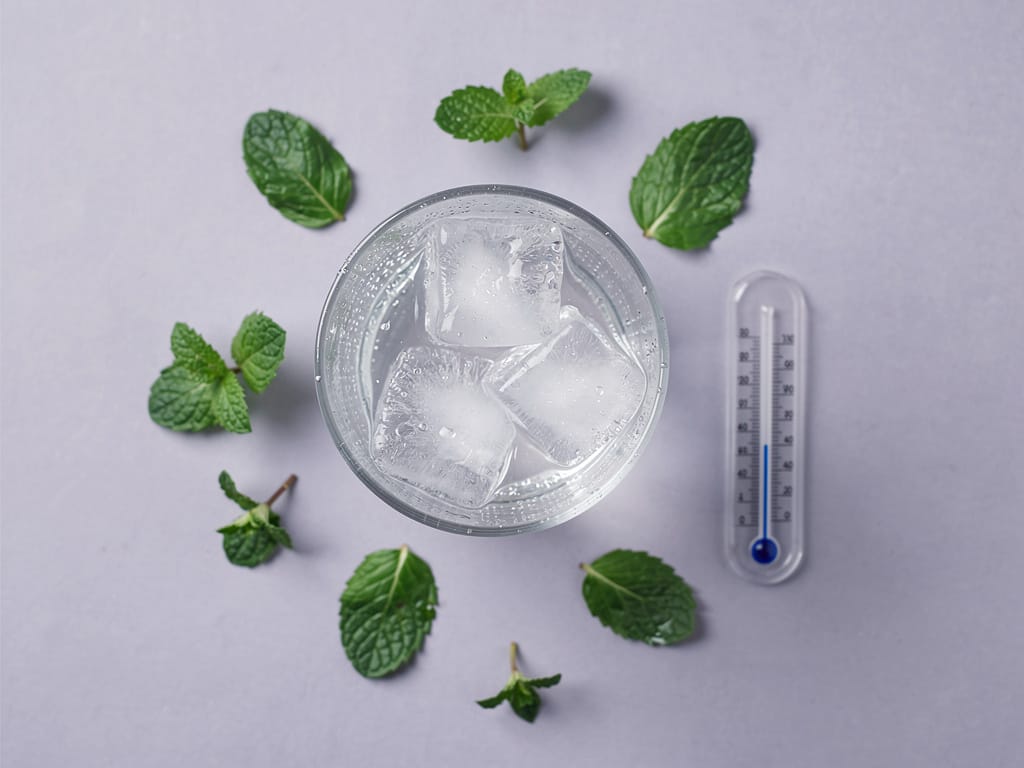 Glass of cold water with ice and condensation on a light background