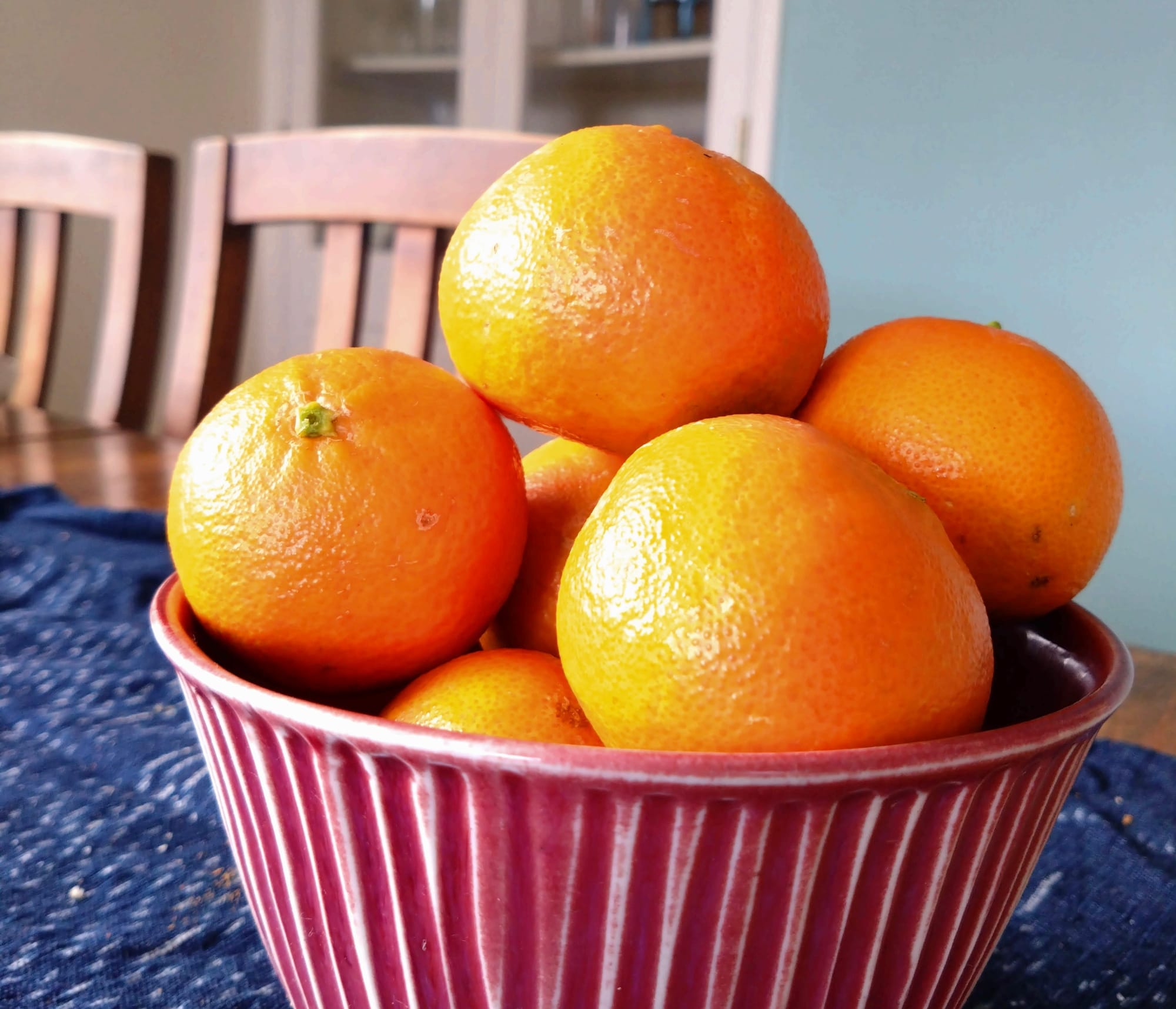 Photo of a red bowl containing 6 bright orange mandarins. 