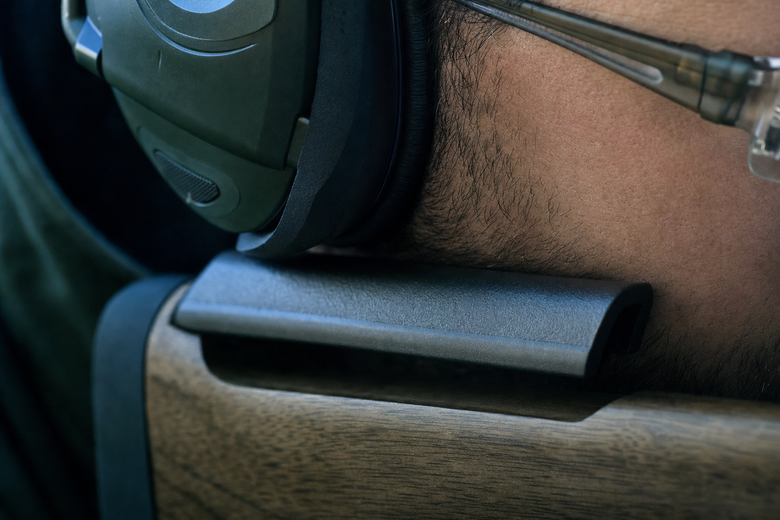 A close detail of a low-profile earmuff cushion, glasses temple, jawline, and a plausible rifle stock comb.