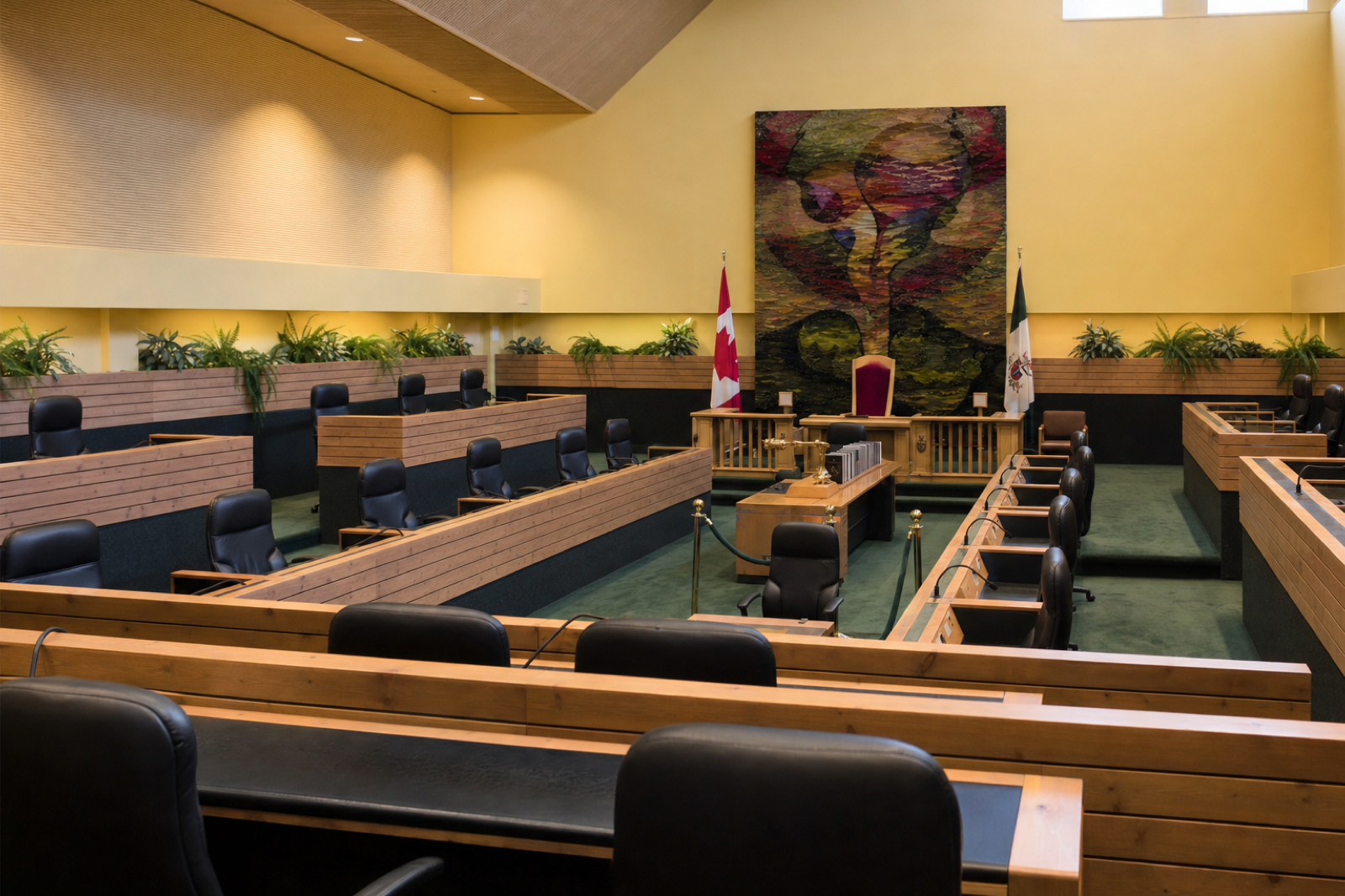 Empty timber desks and dark chairs face the speaker’s platform in the Yukon Legislative Assembly chamber.