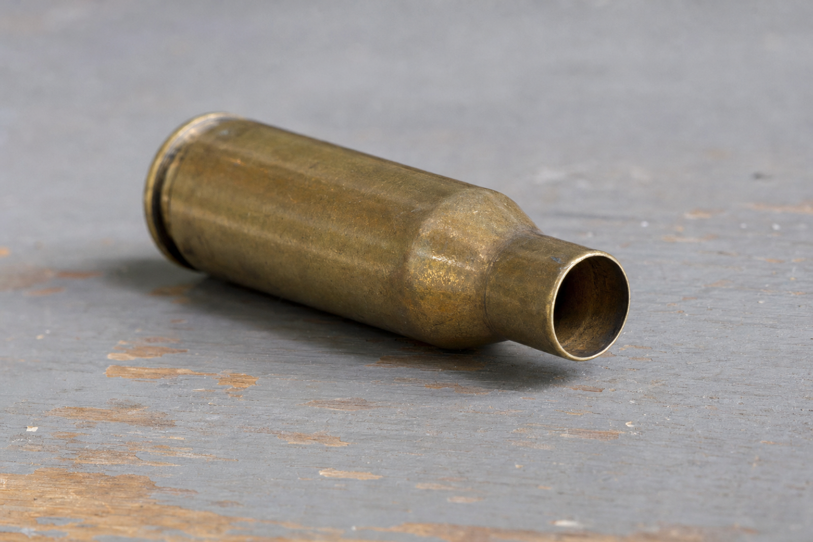 An empty brass case lying on its side, seen at an angle into the open mouth with the neck and shoulder behind it.