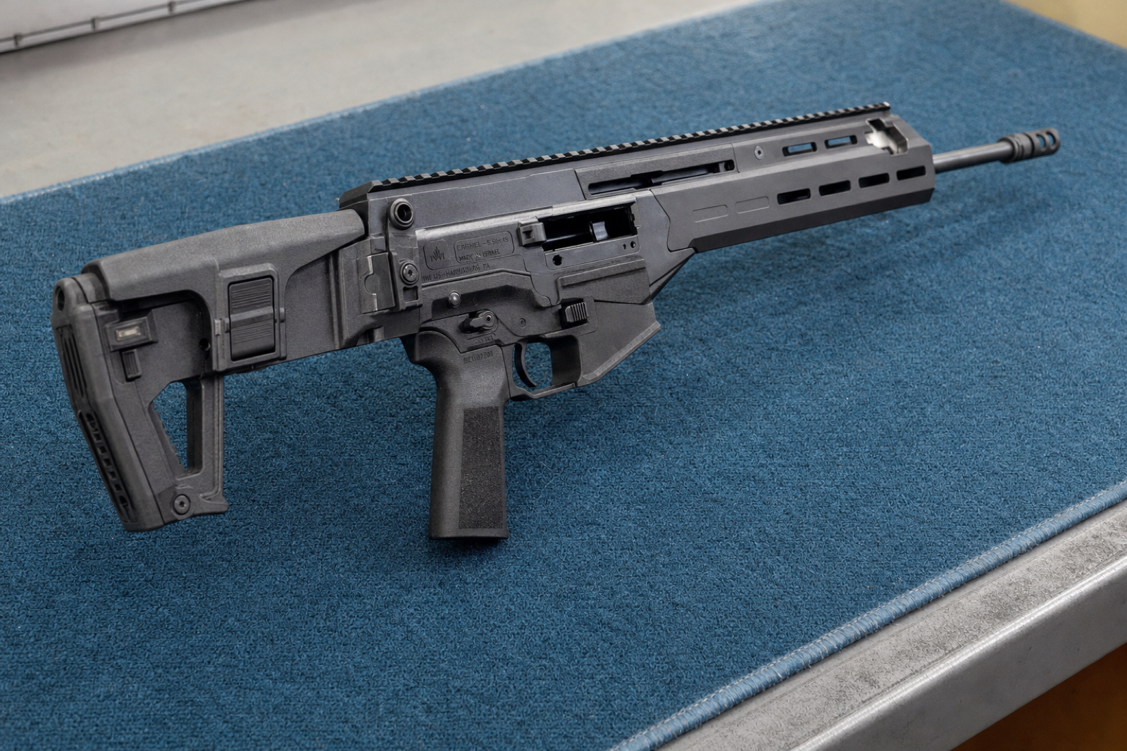 Close oblique view of a black Carmel receiver, trigger guard, top rail and barrel on a blue inspection mat.