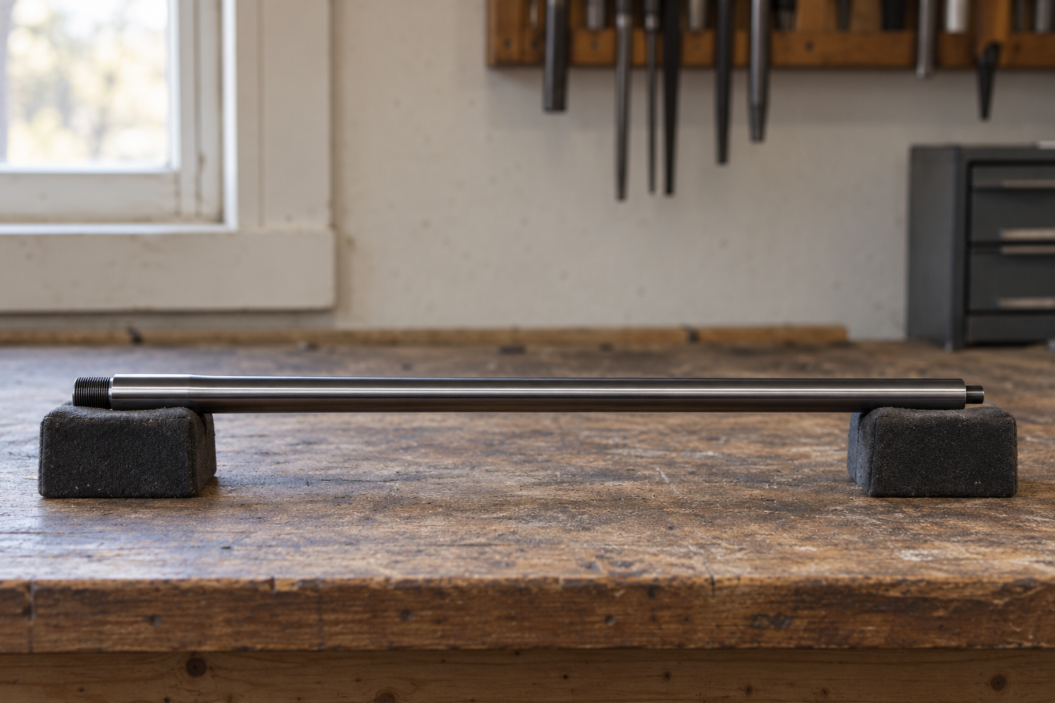 A detached rifle barrel rests horizontally on two padded supports on a workbench.