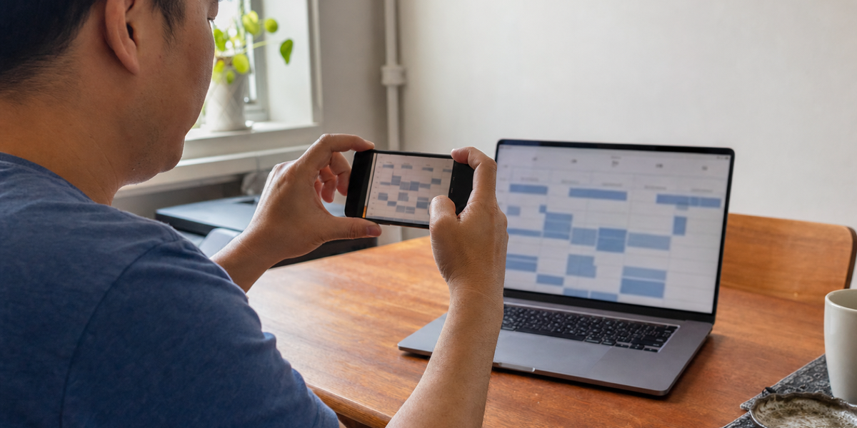 A person photographs an unreadable appointment grid on a laptop in a modest apartment.