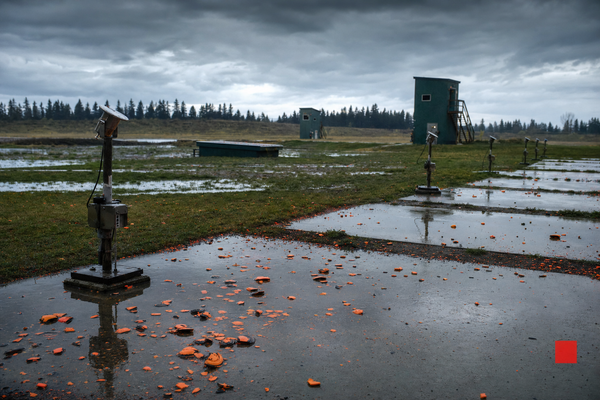 A wet Canadian trapshooting field with concrete stations, trap houses, and orange clay fragments after hard rain.