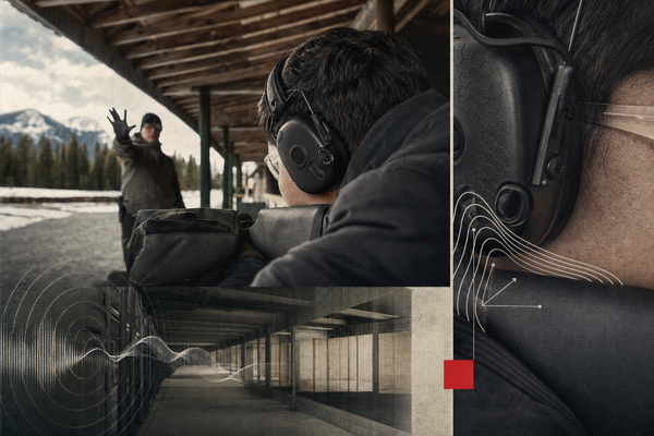 An adult wearing low-profile electronic earmuffs at a covered Canadian firing line, listening toward a range officer while maintaining a stable cheek weld.