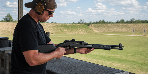 A range worker checks an exact PSA 570 pump shotgun at an empty outdoor test bay.