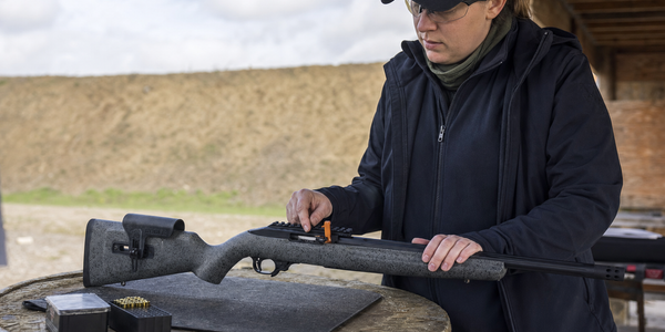 A volunteer checks an open .22 LR rifle at an empty outdoor shooting bay.