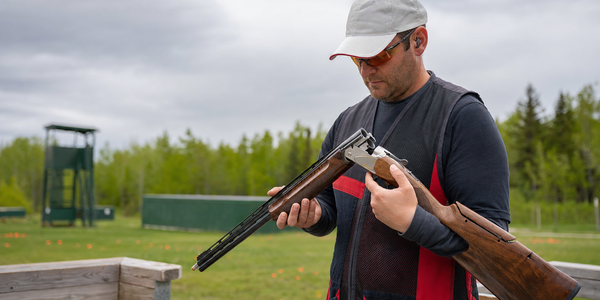 A trap athlete safely checks an open over-under shotgun before a relay.