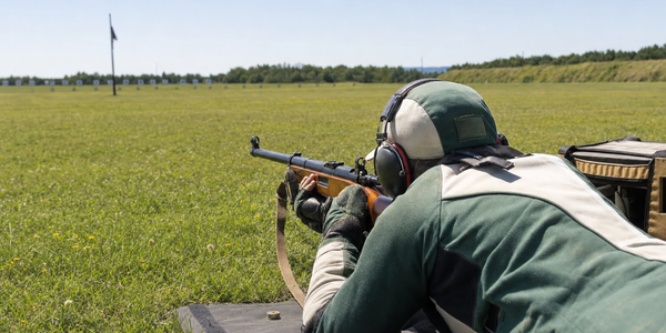 A prone Target Rifle shooter aims through aperture sights on a long outdoor range.