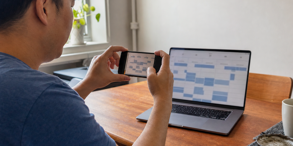 A person photographs an unreadable appointment grid on a laptop in a modest apartment.